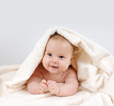 Smiling baby peeks out from under a blanket