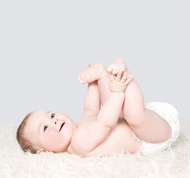 Smiling baby lies on a blanket and plays with his feet